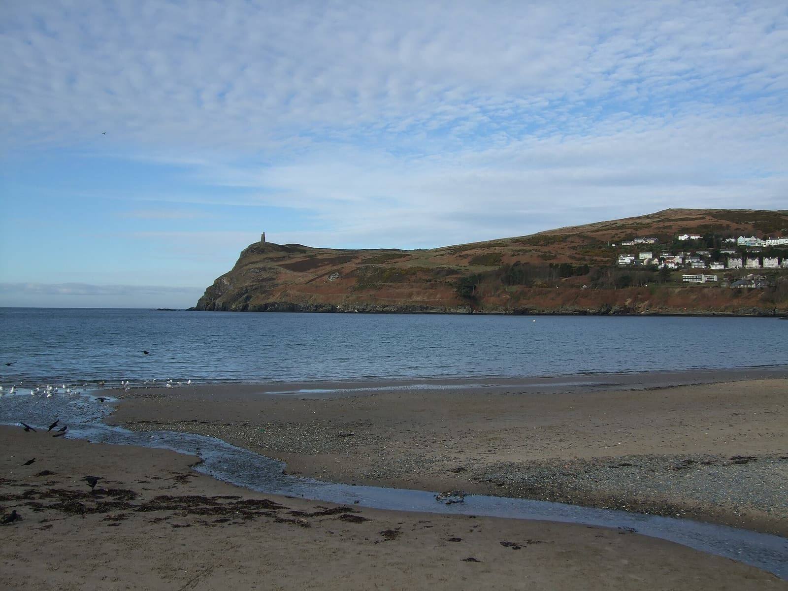 Port Erin's sandy beach at low tide, with the headland of Bradda Head and Milner's Tower across the water.