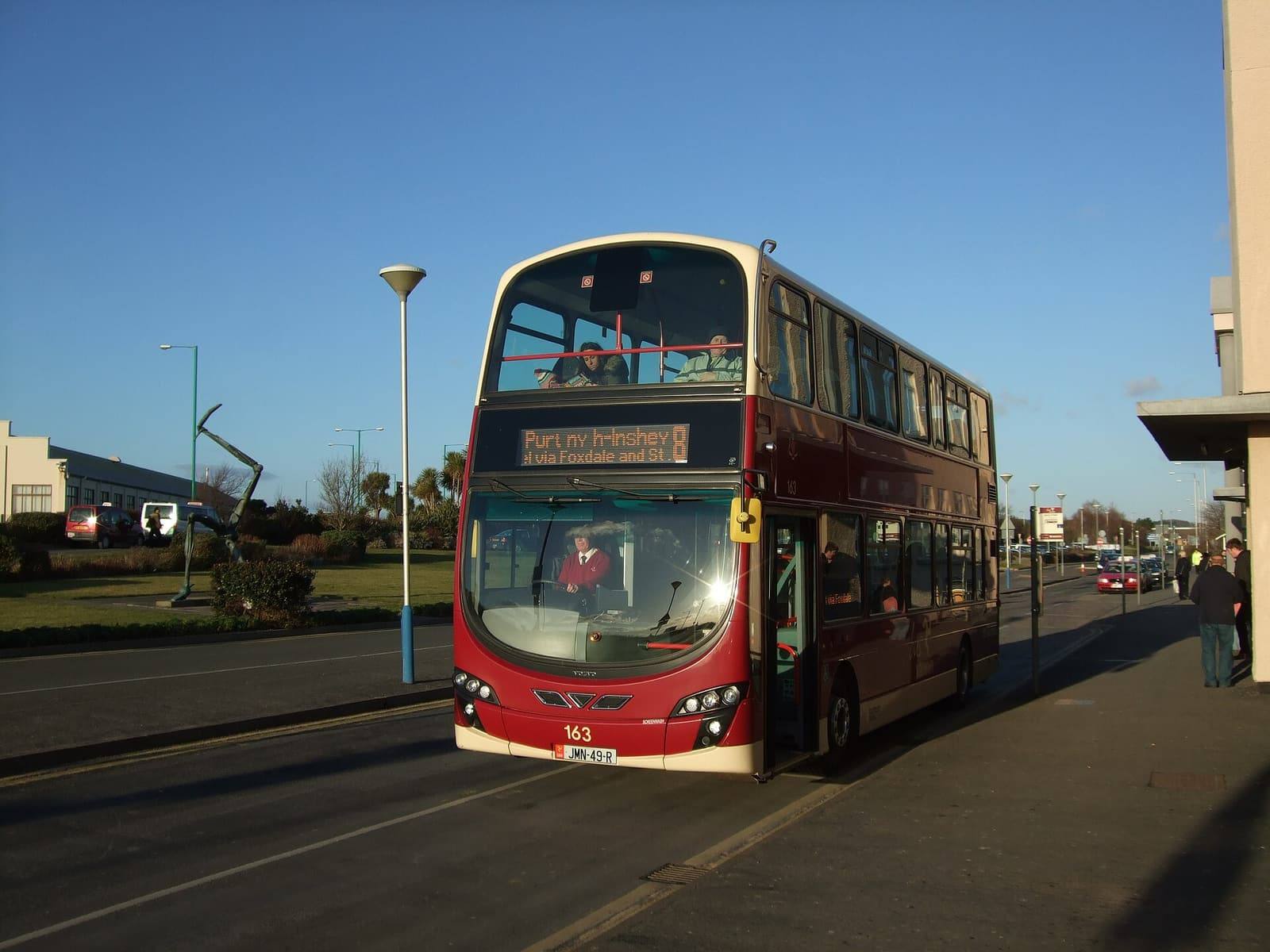 A red Bus Vannin double-decker on its way to Peel waiting at Ronaldsway Airport in low winter sun.