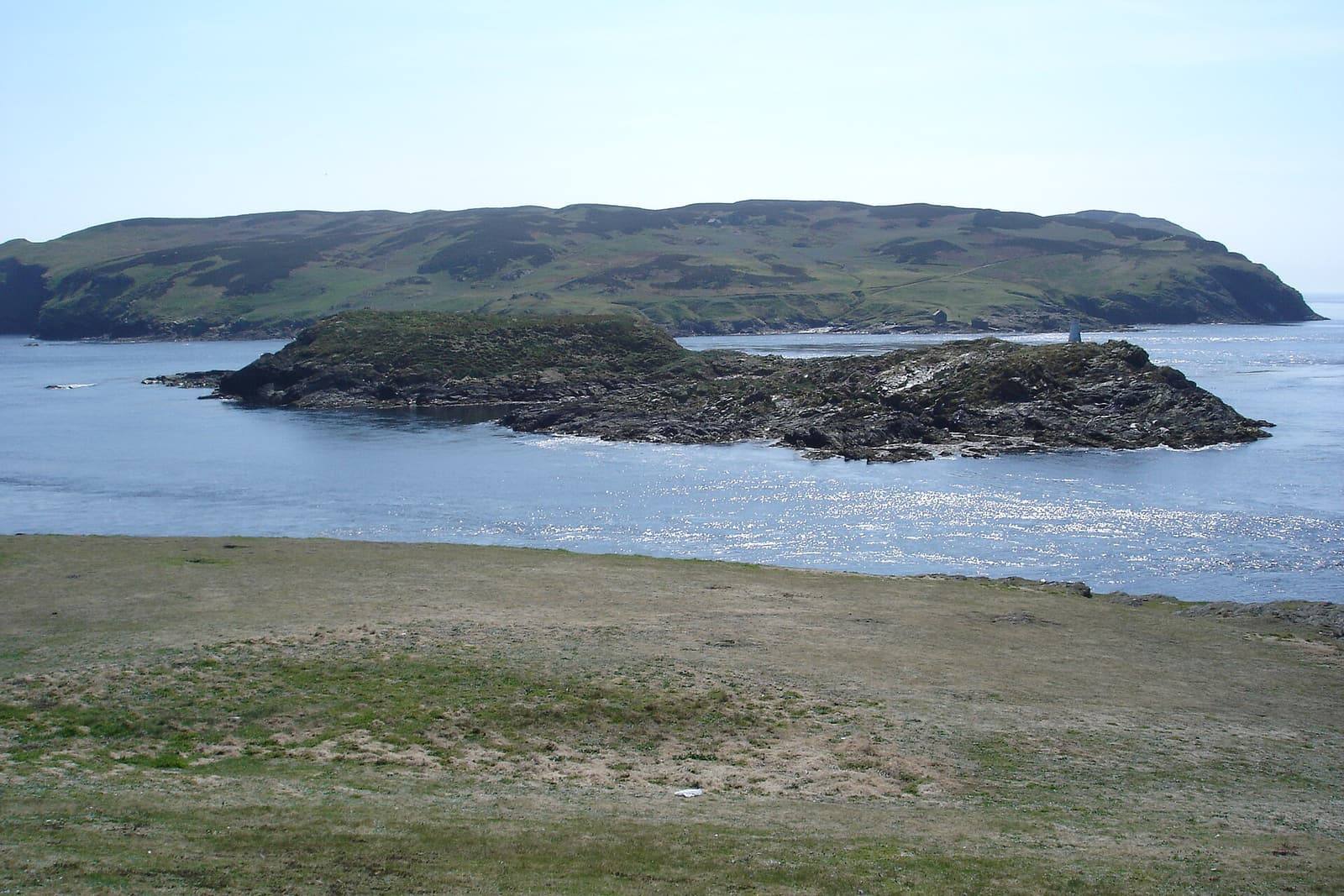 The green hump of the Calf of Man across the bright blue water of Calf Sound, with Kitterland's rocks in between.