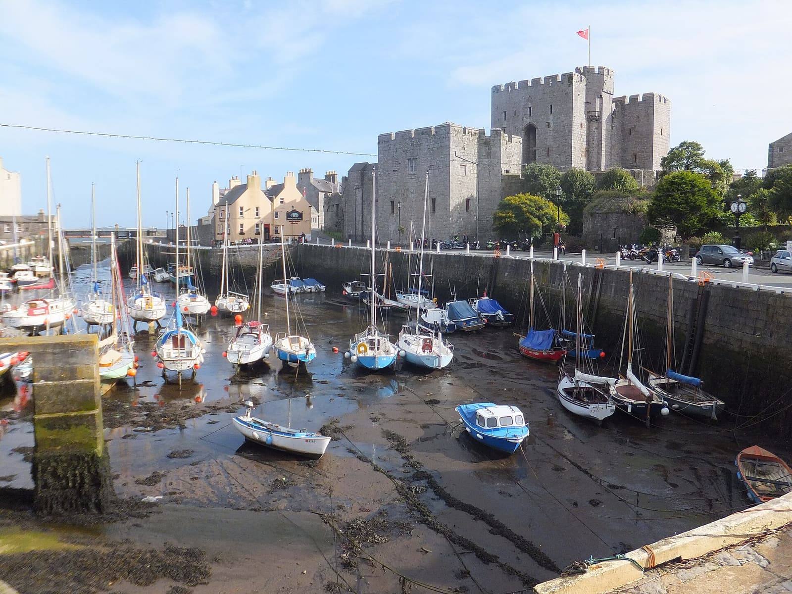 Yachts and small boats on the sand of Castletown harbour at low tide, with the walls and towers of Castle Rushen behind.