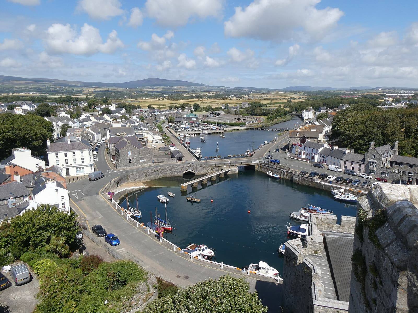 Looking down from Castle Rushen over Castletown's harbour, quays and grey stone buildings, with fields and hills beyond.