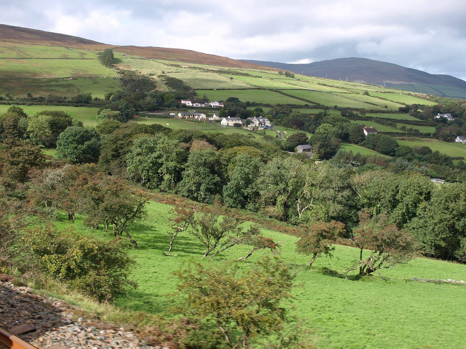 Green fields, hedges and woodland rolling down the valley around Dhoon Glen, with hills and white farmhouses beyond.