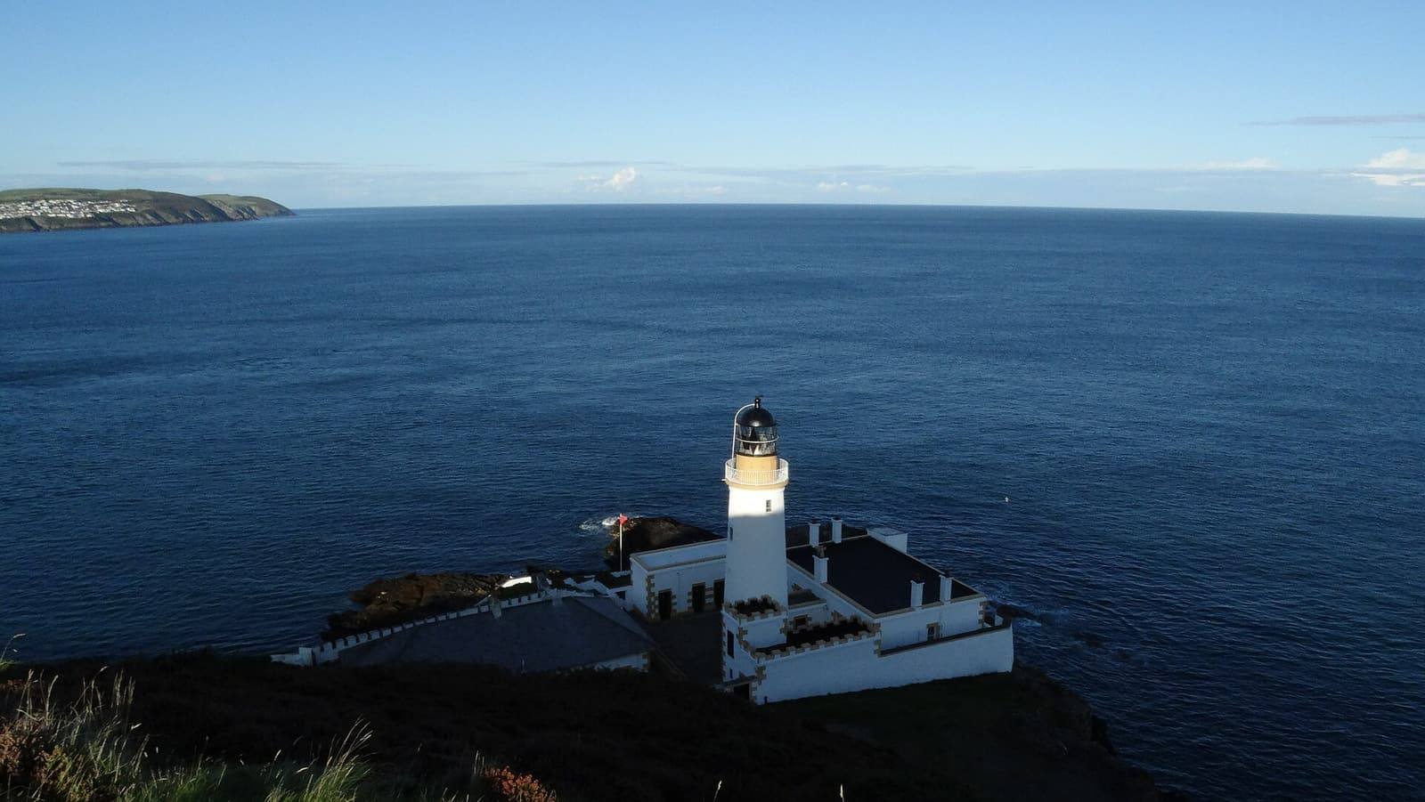 The white Douglas Head lighthouse on dark cliffs above a calm blue sea.