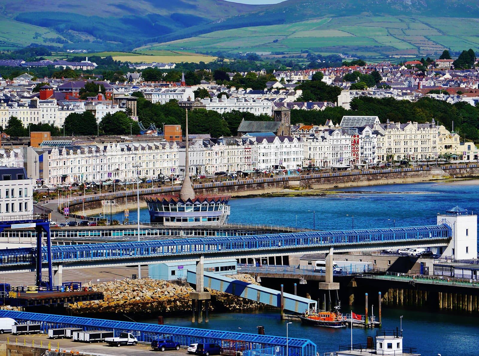 Rows of white seafront buildings along Douglas promenade above the harbour and the Sea Terminal, with hills behind.