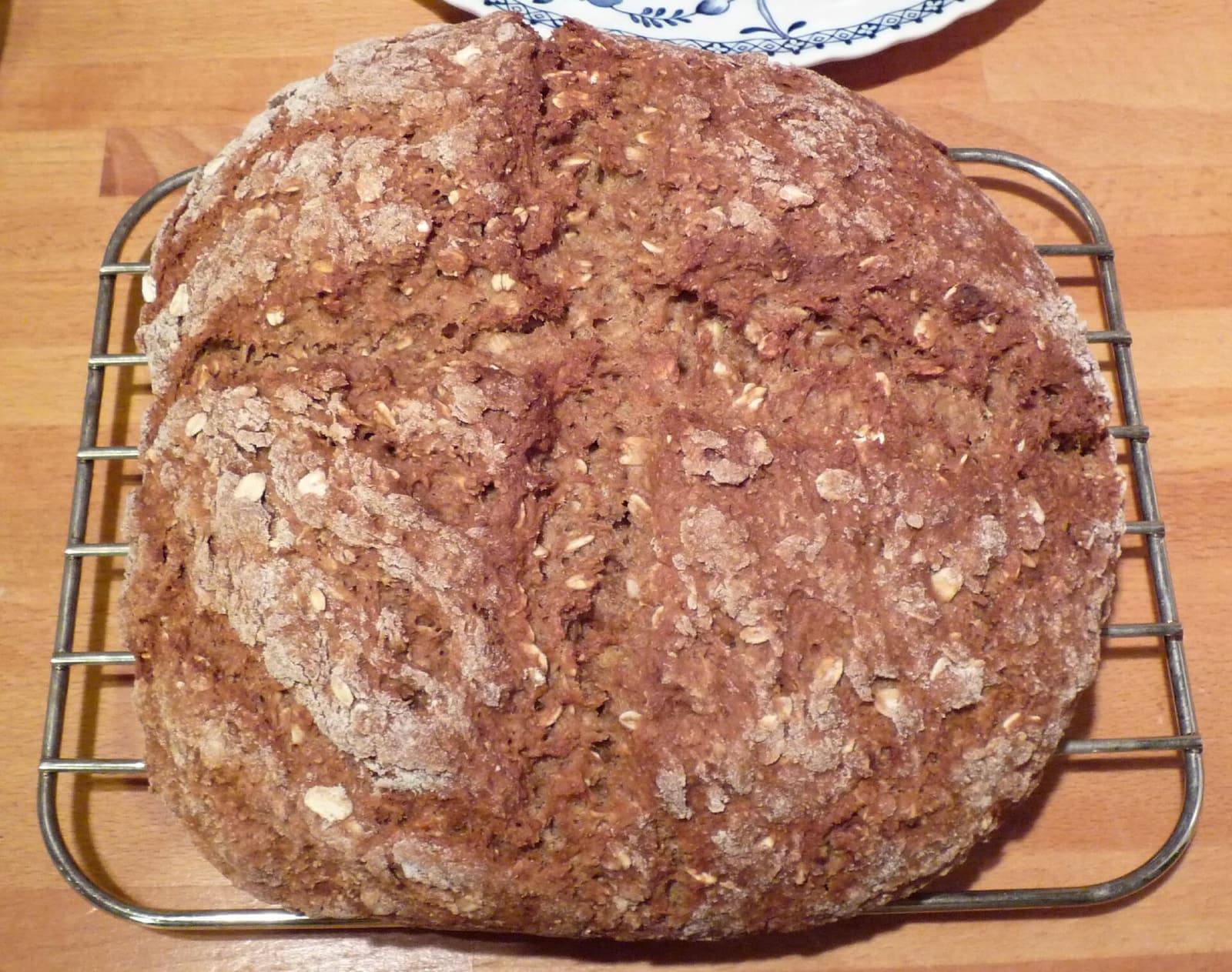 A round, cross-scored soda loaf with a floury, oat-flecked crust cooling on a wire rack.