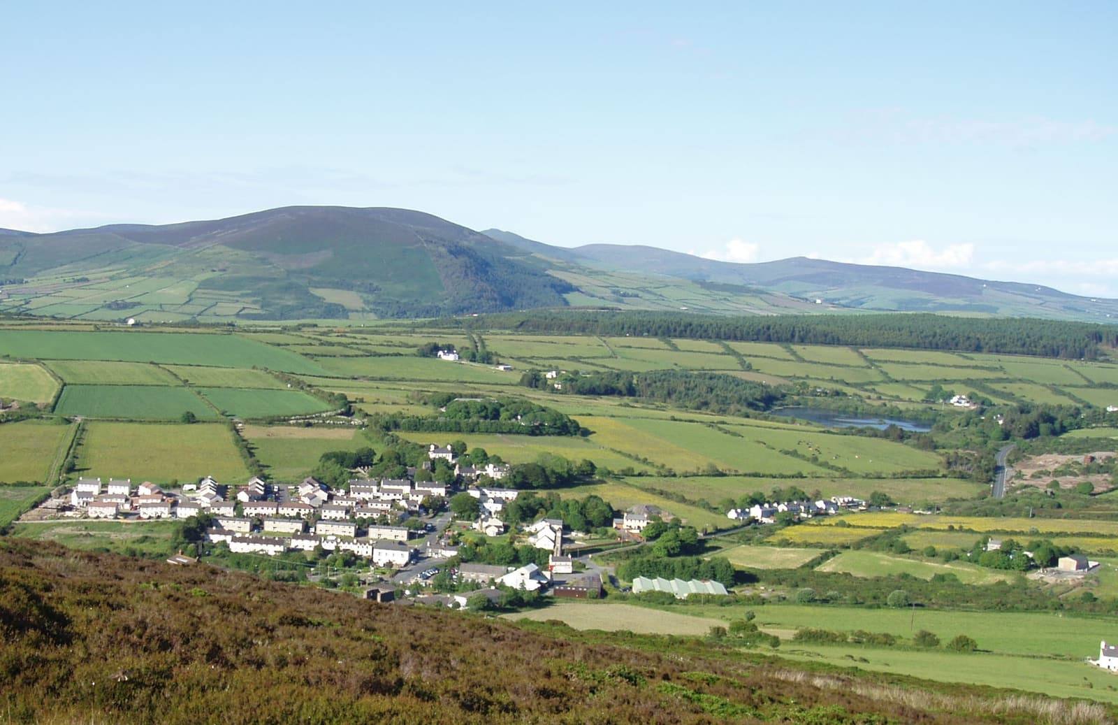 The village of Foxdale among green fields and hedges, with rolling hills and the central valley beyond.