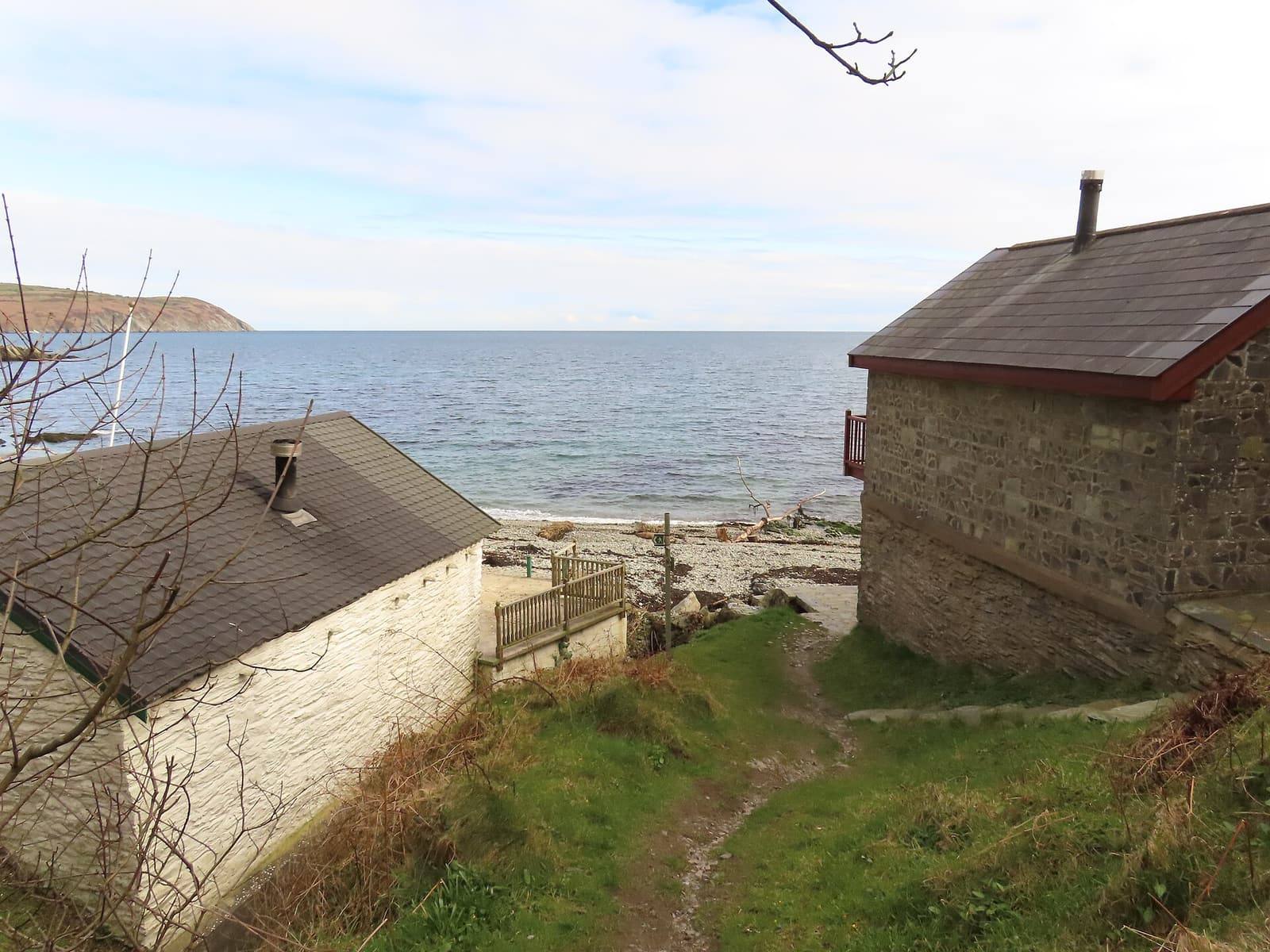 The pebble shore of Garwick Bay between two stone cottages, with the sea and a headland beyond.