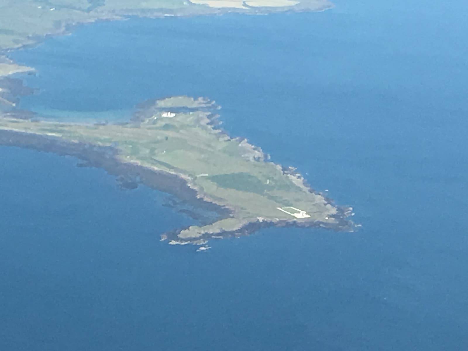 The long, low Langness peninsula reaching into a blue sea, seen from the air.