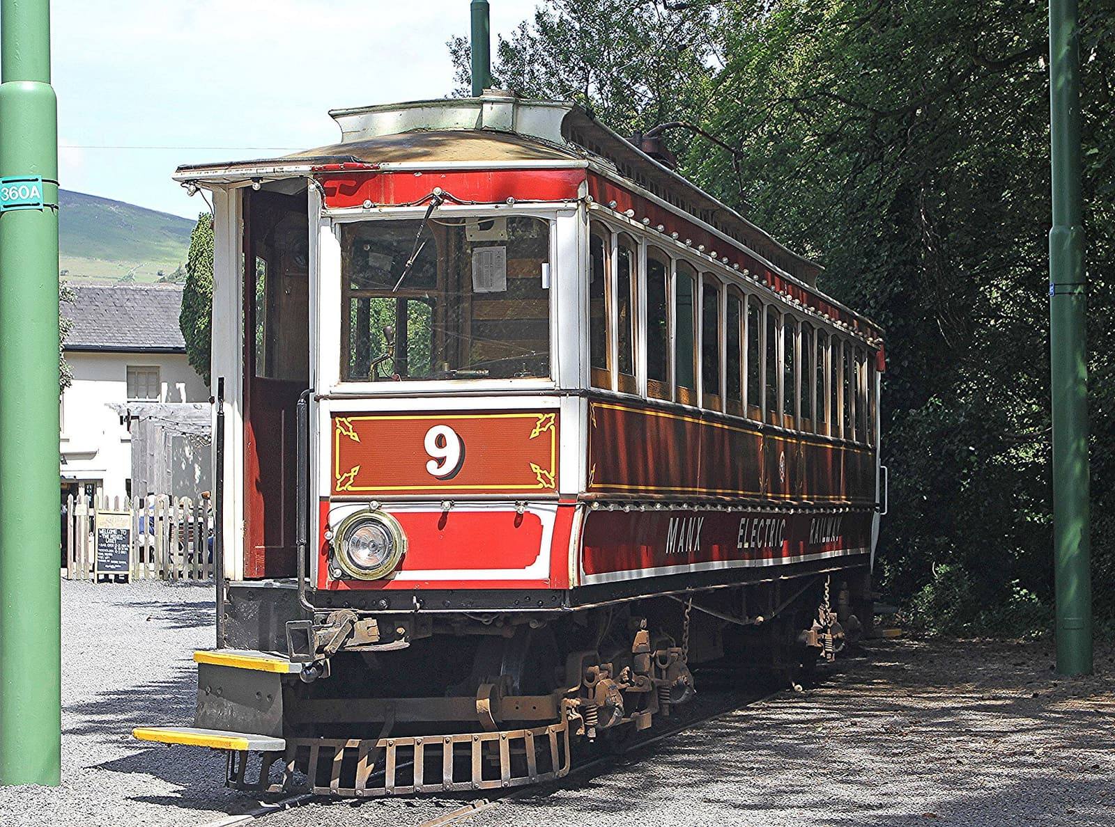 A red and varnished-wood Manx Electric Railway tram car standing at Laxey station among trees.