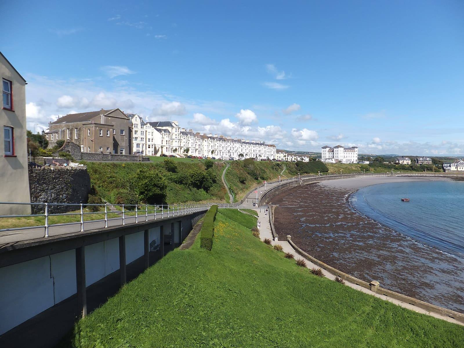 The curve of Chapel Bay at Port St Mary, with the promenade's terraces above the beach on a sunny day.