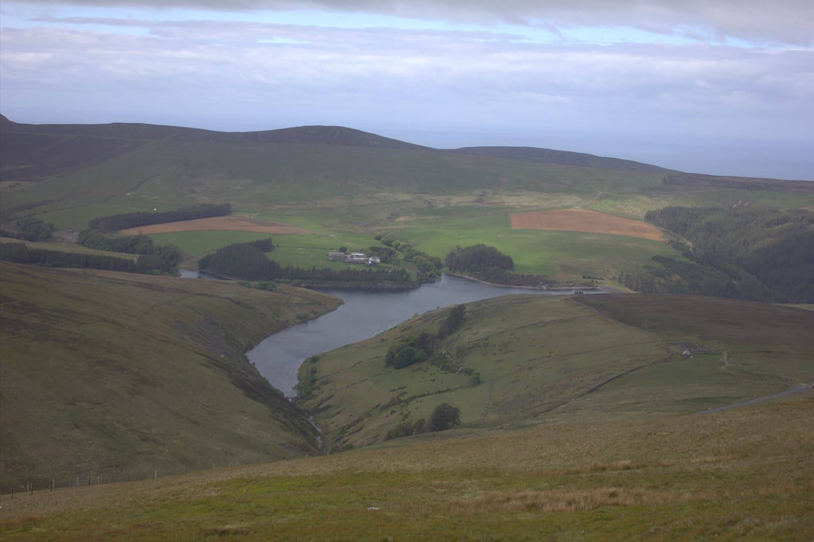 Sulby reservoir winding between rolling brown and green hills under a wide sky.
