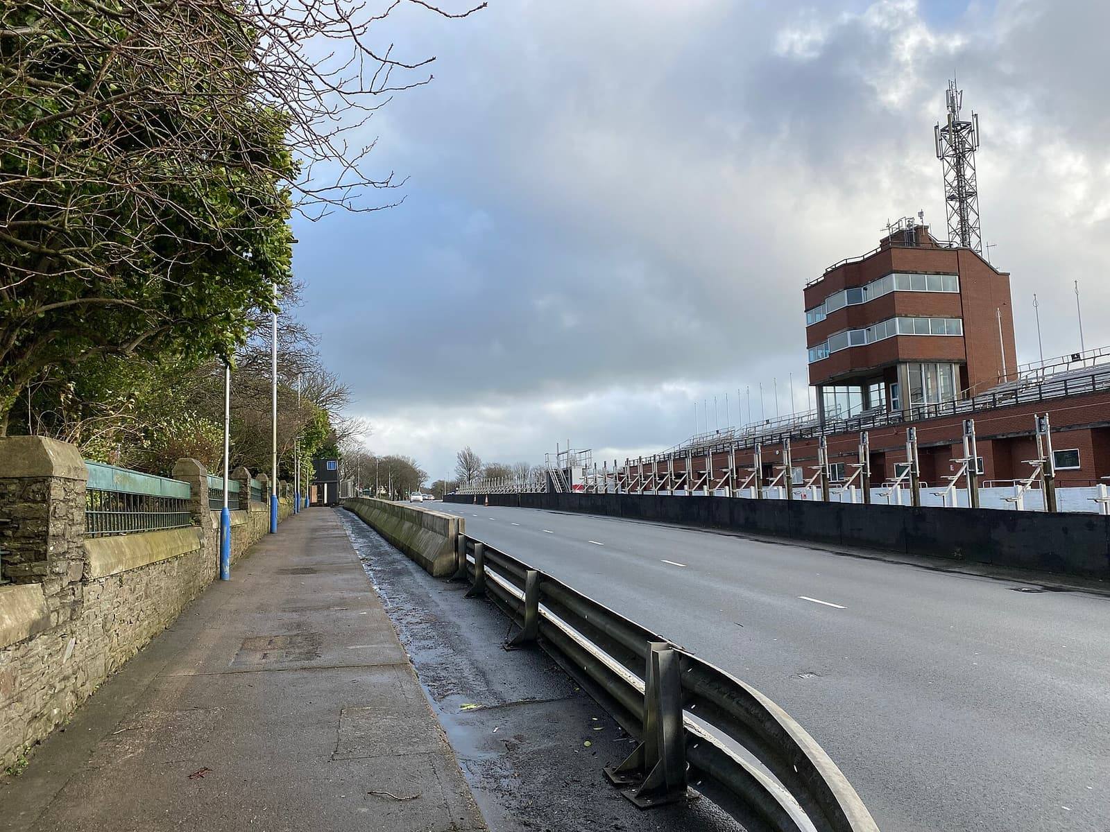 Glencrutchery Road in Douglas running past the TT Grandstand and its tower, with barriers along the kerb.