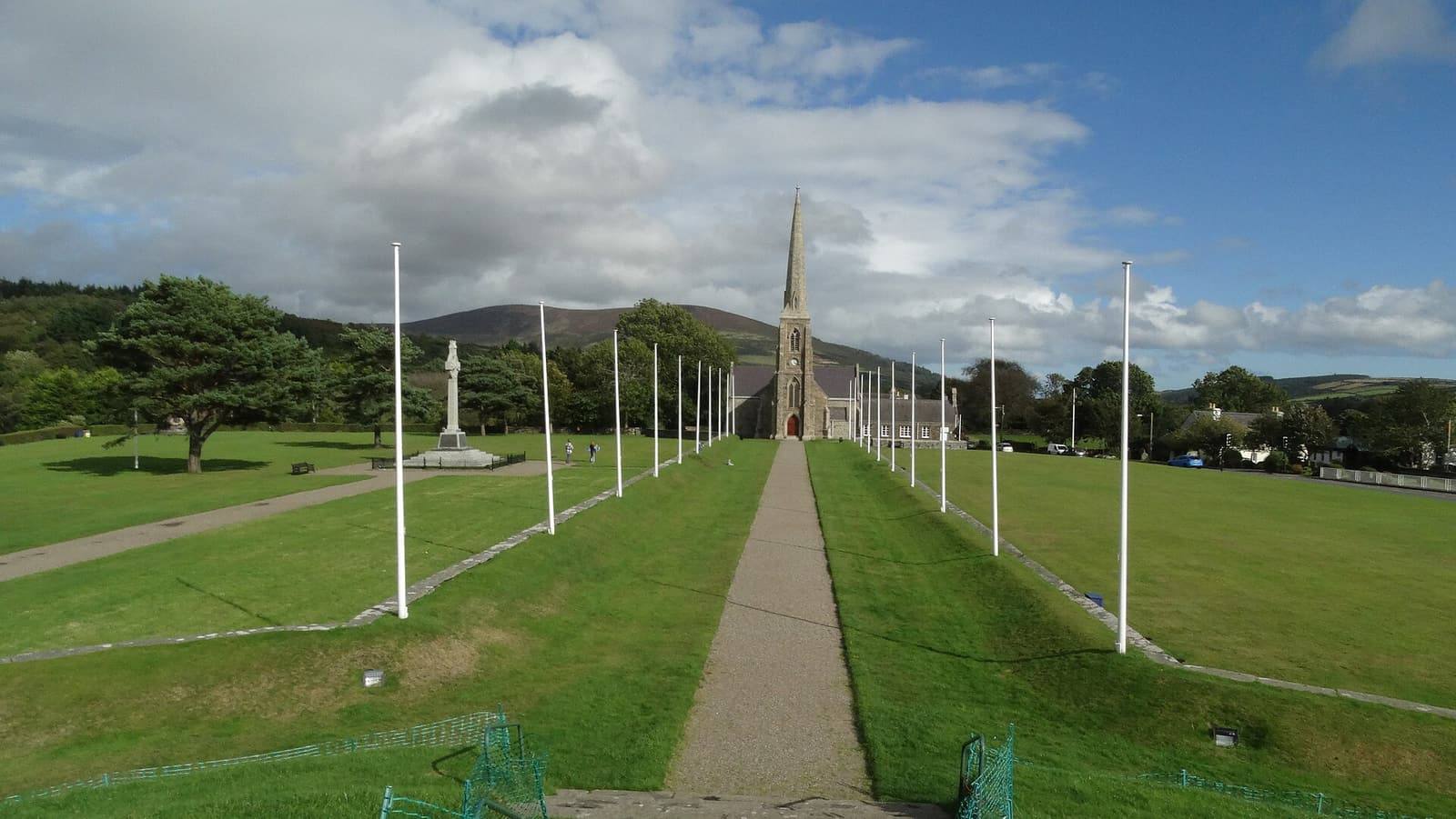 The straight processional path at St John's, lined with flagpoles, leading to the spire of the Royal Chapel of St John the Baptist.